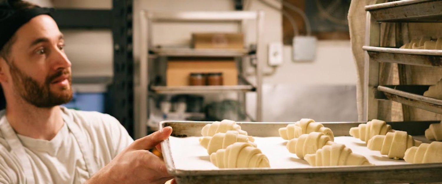 Un boulanger sort une plaque de croissants crus du chariot