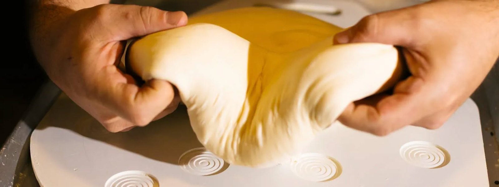 Les mains d'un boulanger étirant une pâte sur le plan de travail